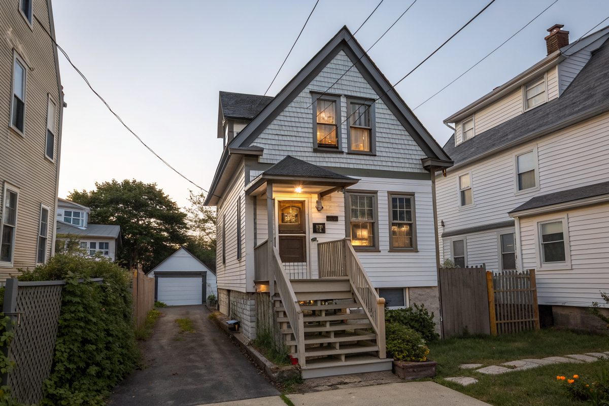 A narrow frame cottage raised over a lower living unit, with a steep front gable and side stairs